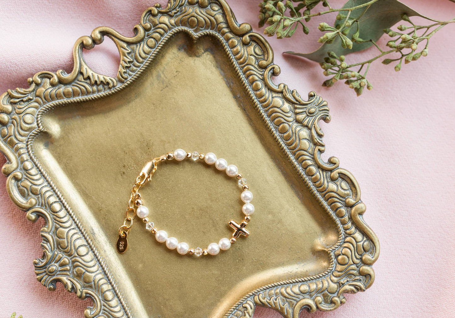 Pearl bracelet with a gold clasp on an ornate gold tray with a pink background